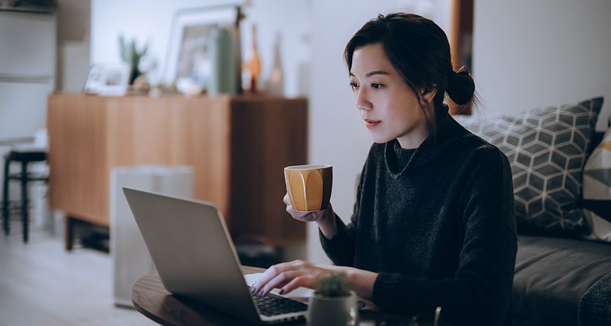 woman with a cup of coffee working remotely on a laptop