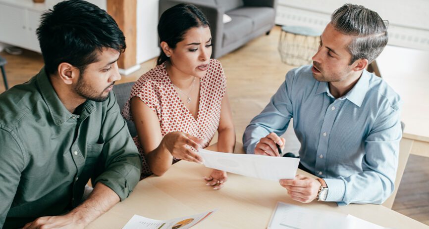 Two men and one woman, sitting at a table, reviewing a document.