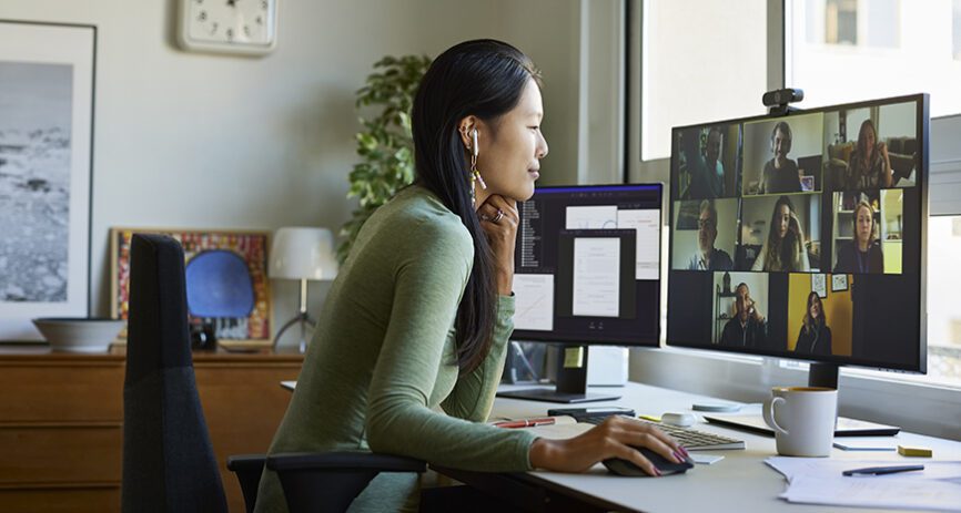 A women leans in to her computer that displays numerous co-workers in a meeting.