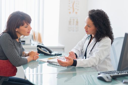 A woman is meeting with her doctor at the doctor's office. They are sitting across from each other at a desk and the doctor appears to be going over notes.