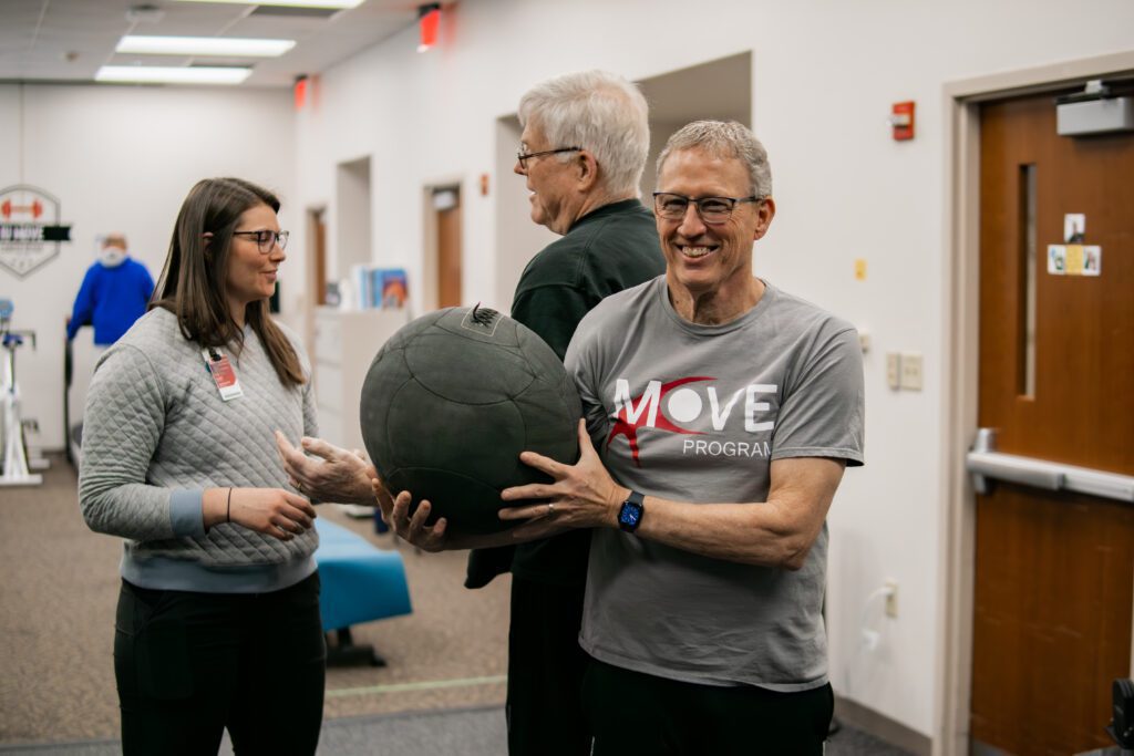 Older man holding exercise ball and smiling. 