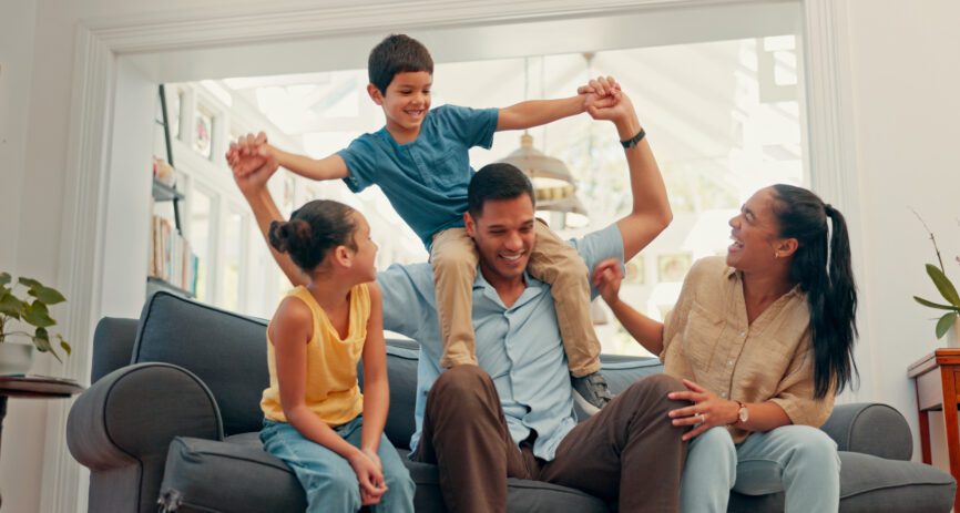 Young family on their sofa and the dad has the son on his shoulders.