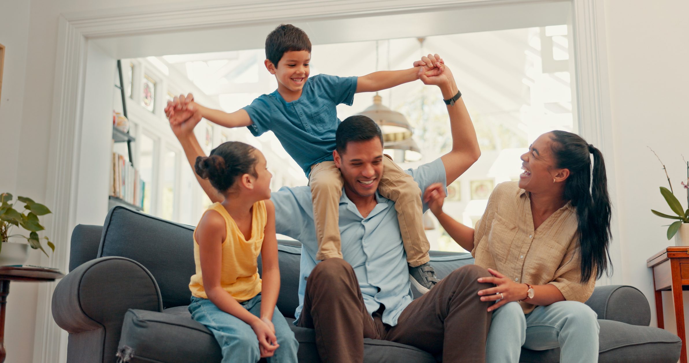 Young family on their sofa and the dad has the son on his shoulders.