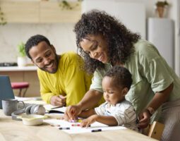 Smiling parents spend time coloring with toddler son at home.