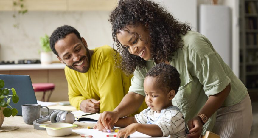Smiling parents spend time coloring with toddler son at home.