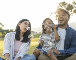 Happy parents blow bubbles with child outside