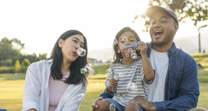 Happy parents blow bubbles with child outside