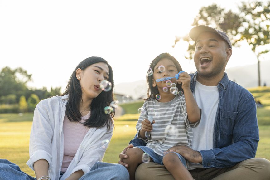 Happy parents blow bubbles with child outside